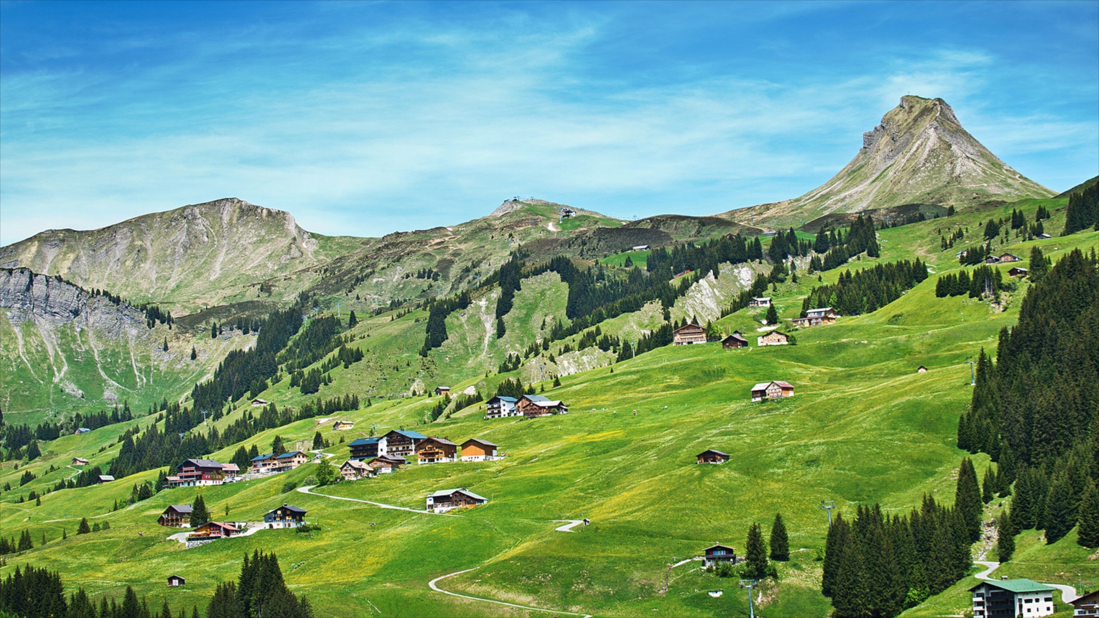 A mountainous landscape with a prominent peak, green valleys, and scattered houses.