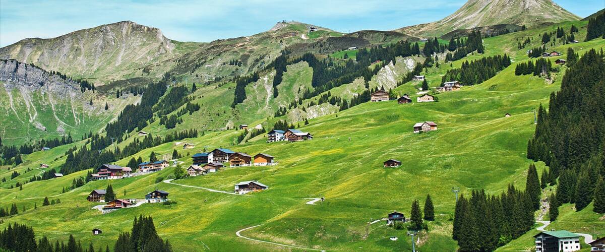 A mountainous landscape with a prominent peak, green valleys, and scattered houses.