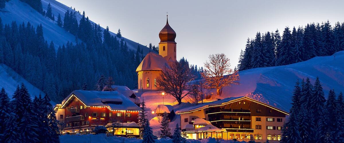 A snow-covered mountain lodge with a church steeple and lit windows.