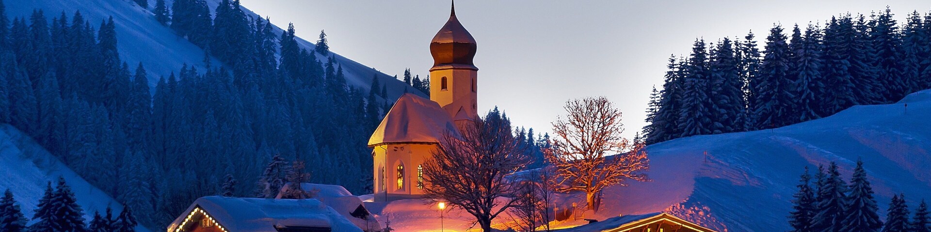 A snow-covered mountain lodge with a church steeple and lit windows.