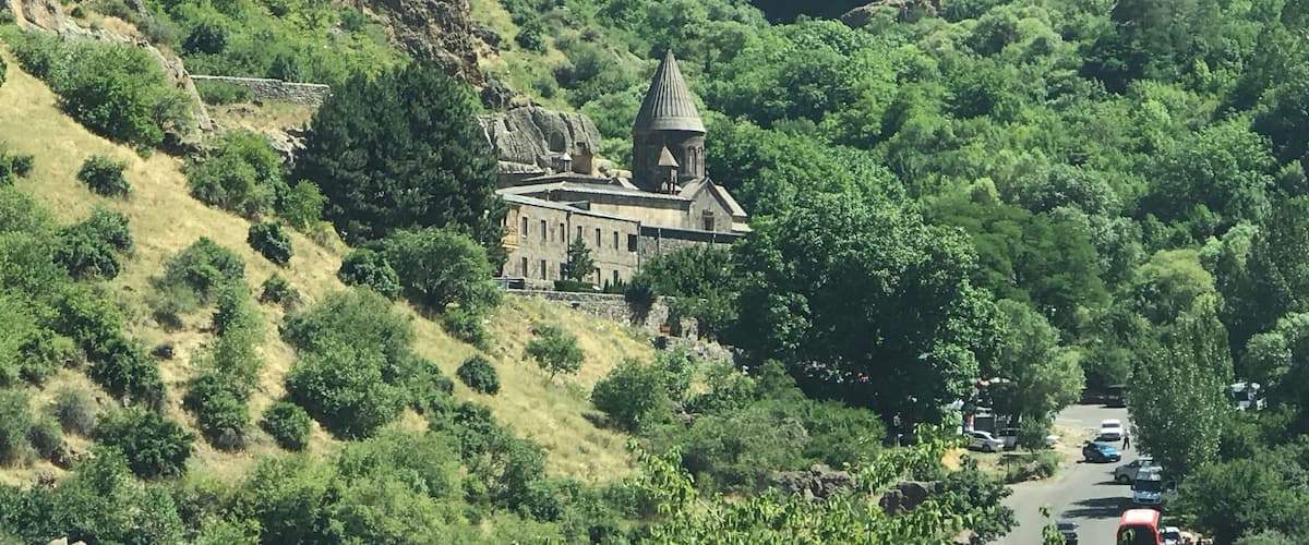 A church with a dome on a hillside surrounded by lush greenery and rocky cliffs.