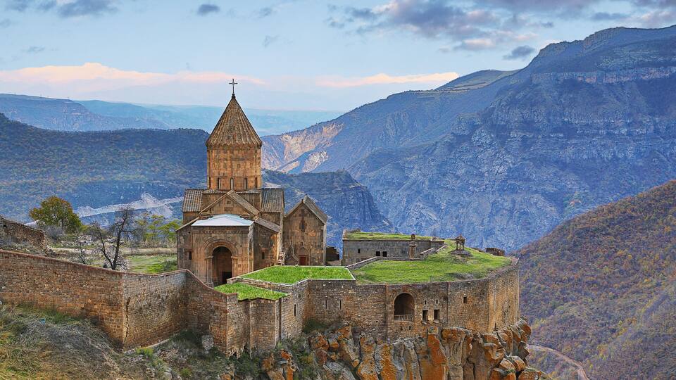A historic stone church with a bell tower on a cliffside overlooking a valley.