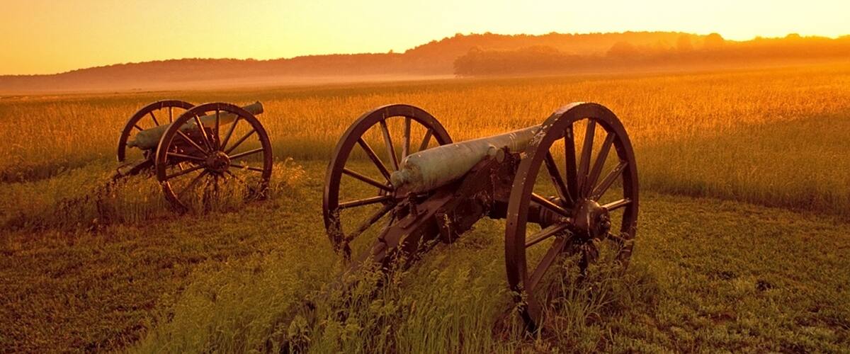 Three old cannons in a field with a sunset in the background.