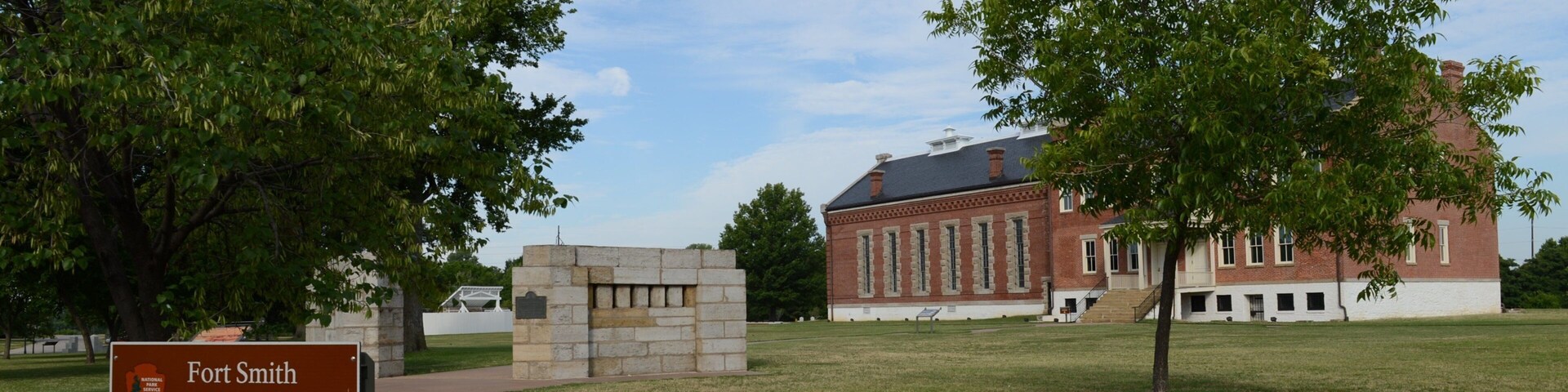 Sítio histórico com centro de visitantes, um edifício de tijolos e árvores ao redor.