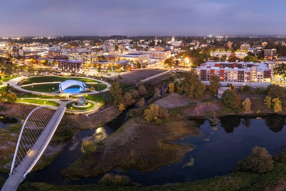 Une vue sur une ville au crépuscule, avec un pont imposant, un parc circulaire doté d’un globe terrestre et une rivière.
