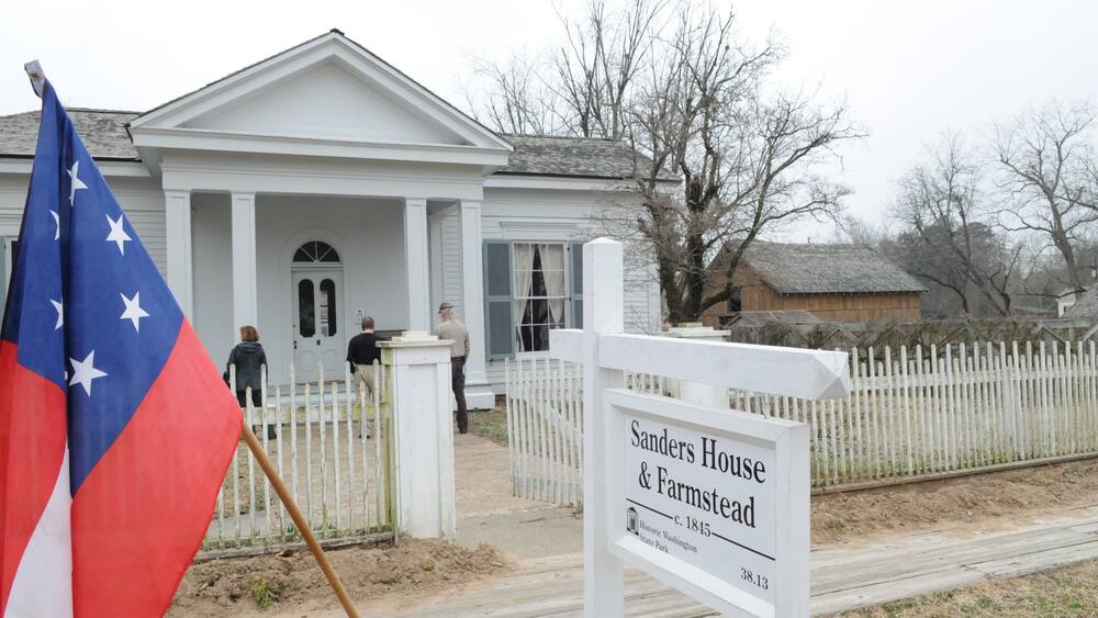 L’extérieur de la maison et de la ferme Sanders, un bâtiment historique datant de 1845, est situé au numéro 38,13 d’une rue bordée d’une clôture en piquets blancs et où flotte un drapeau.
