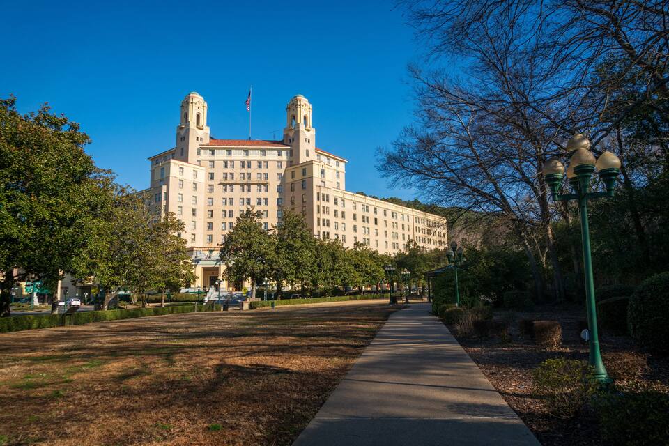 A large beige building with two towers, surrounded by trees and a sidewalk.