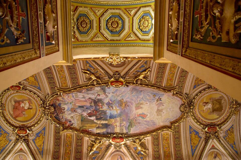 An ornate ceiling with intricate gold and blue designs, a central oval painting, and detailed frescoes.