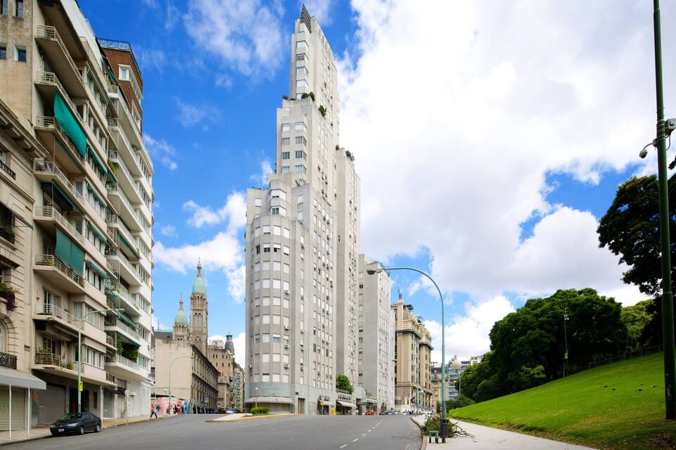A city street with tall buildings, a clear blue sky, and a green park.