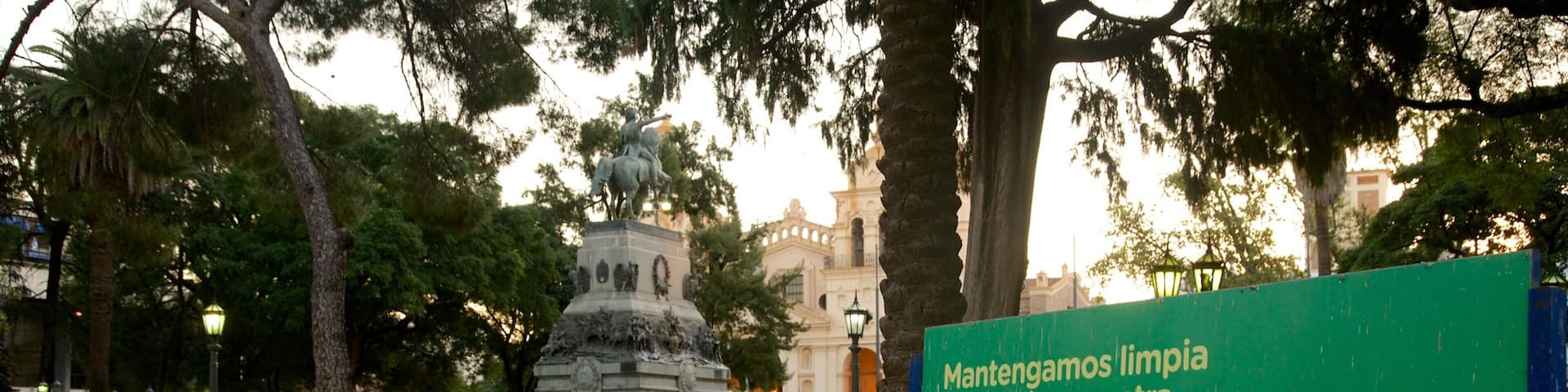 A green sign for Plaza San Martín in a park with a statue and trees.