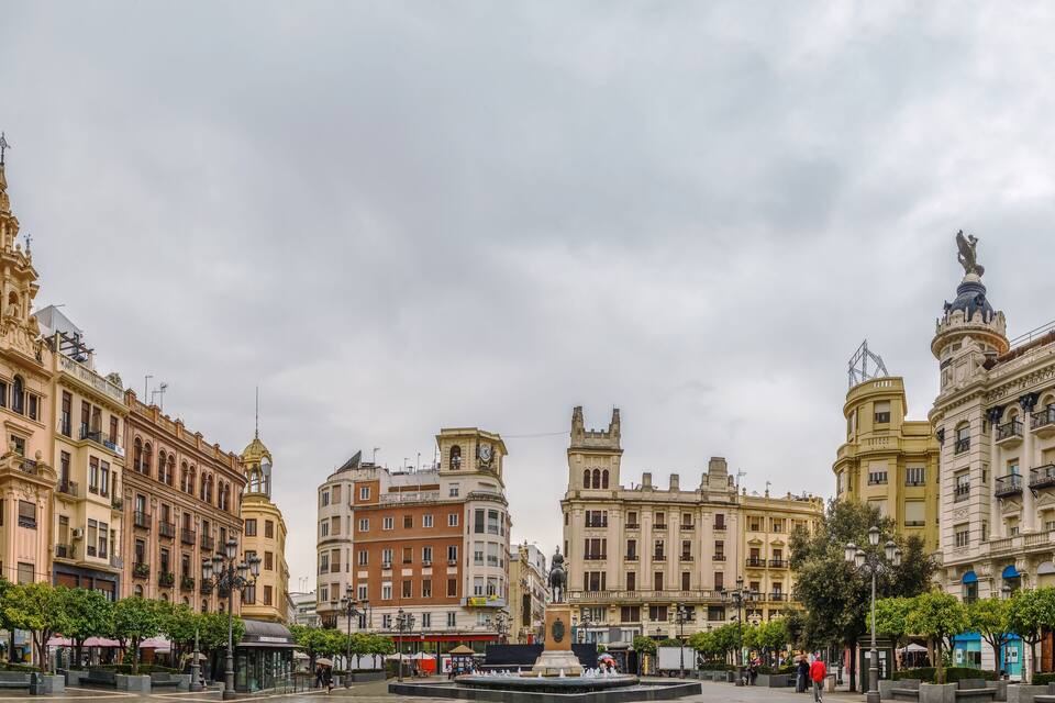 Una plaça històrica amb edificis ornamentals, una font central i una estàtua.