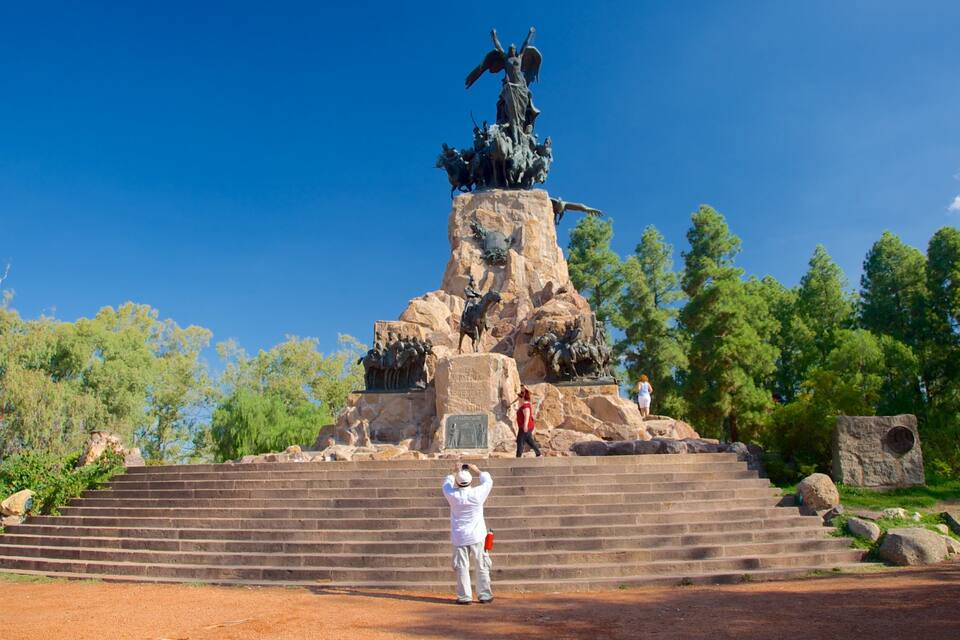A large statue on a pedestal with steps leading up to it, surrounded by trees and a clear blue sky.
