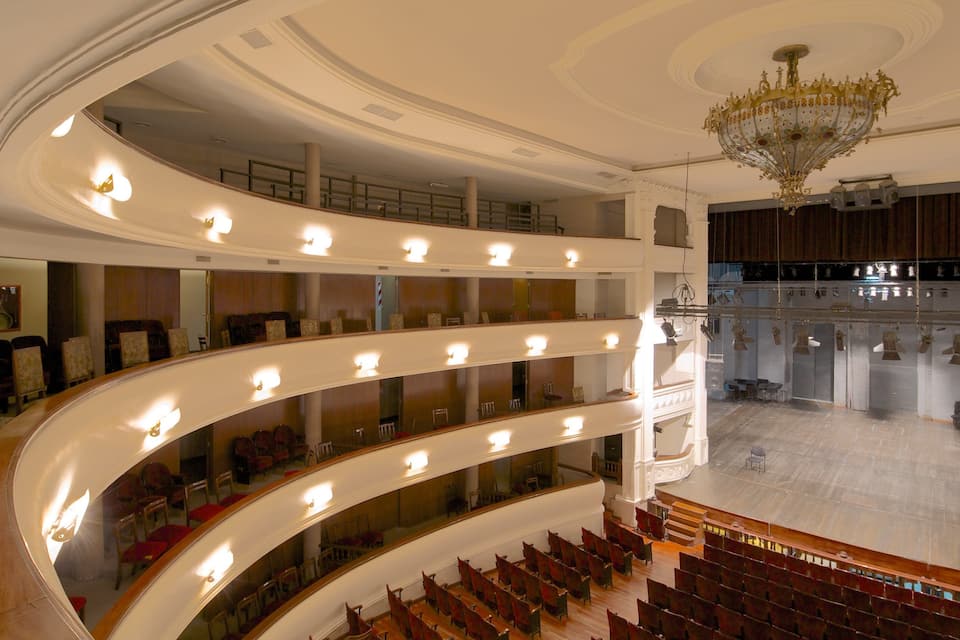 Un ampio auditorium a più livelli, con posti a sedere disposti a gradinate e un sontuoso lampadario.