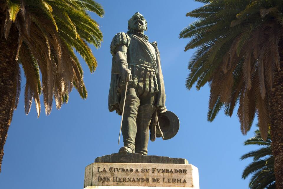 Una estatua de Don Hernando de Lara con espada y escudo, rodeada de palmeras.