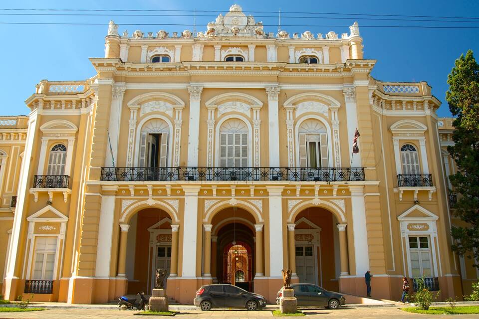 Un edificio neoclásico imponente con columnas ornamentales, una entrada central y un balcón con barandillas decorativas.