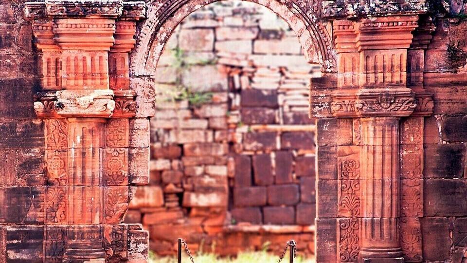 An ancient stone archway with intricate carvings and a chain barrier.