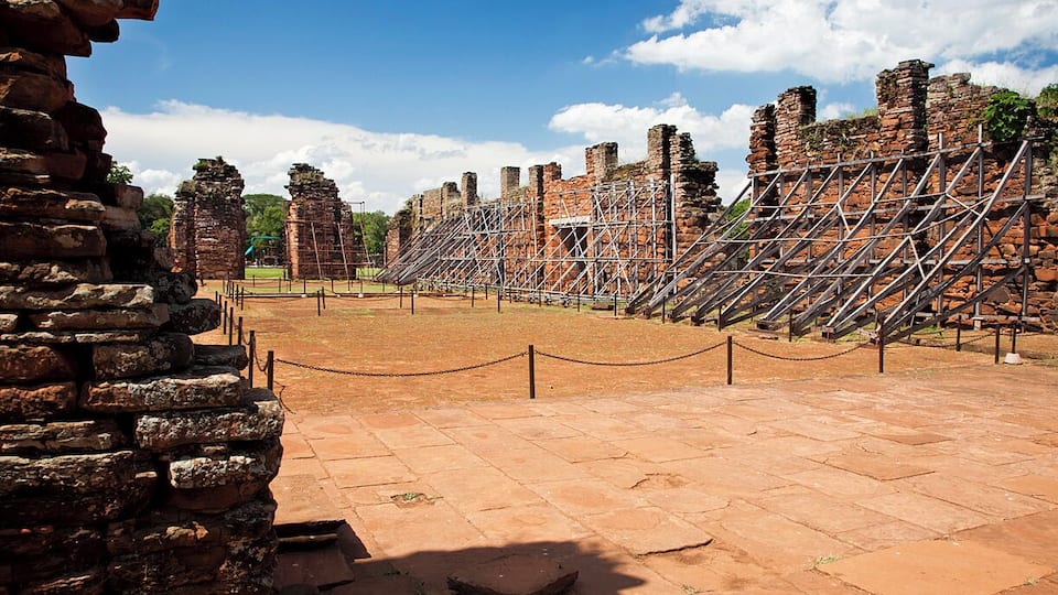 Ancient stone ruins with scaffolding, a clear sky, and a paved walkway.