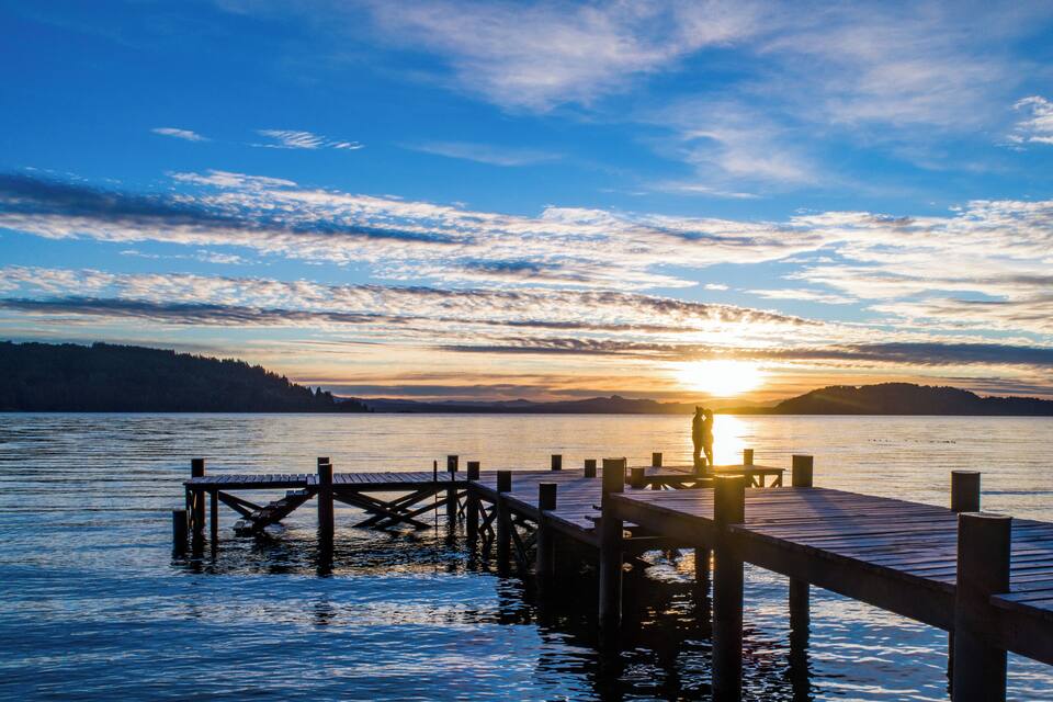 Un muelle de madera que se adentra en aguas tranquilas, con un atardecer de fondo.