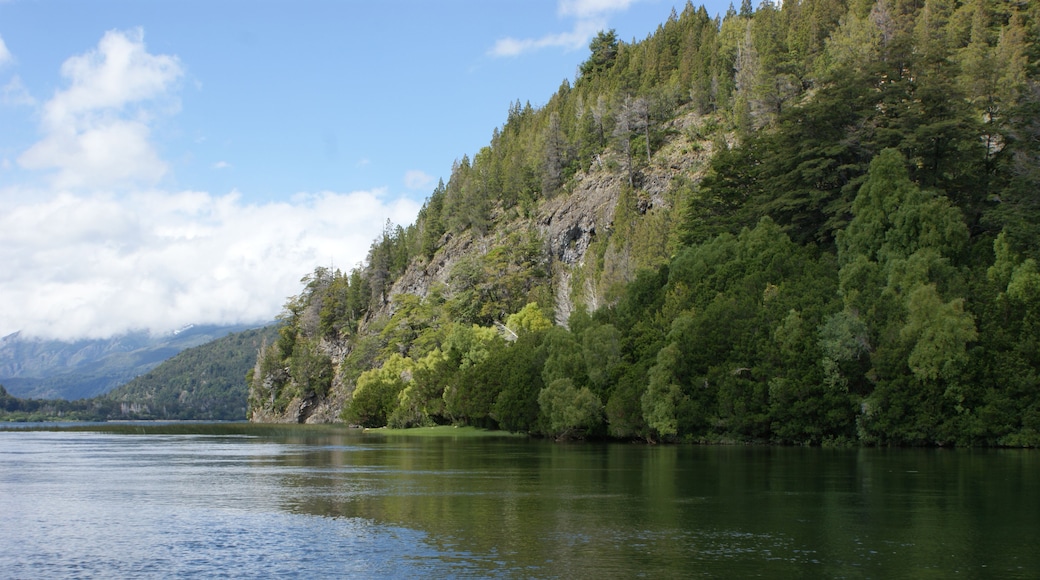 A calm lake surrounded by dense forest and a mountain range in the distance.