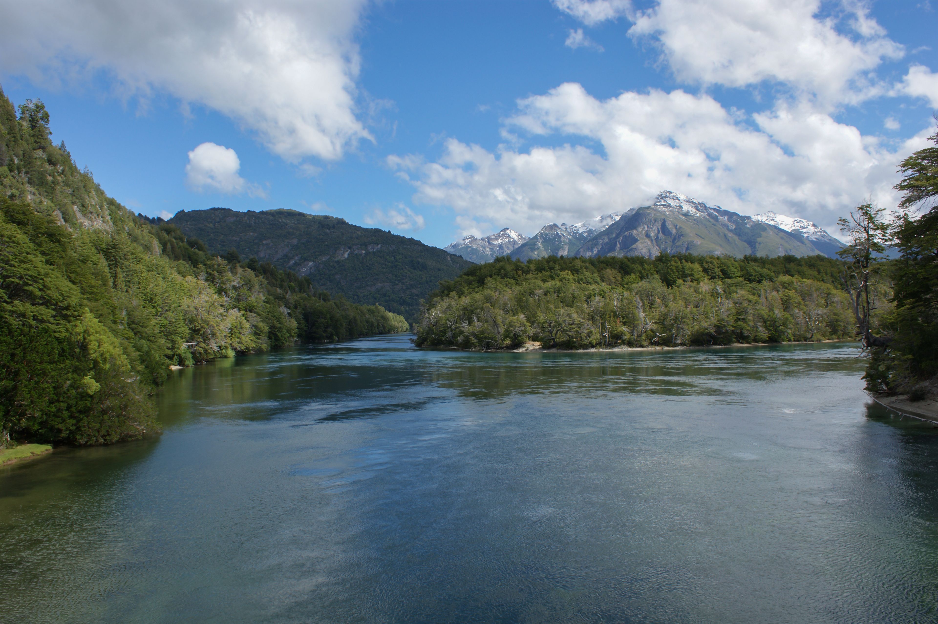 Une rivière qui traverse une vallée boisée, avec des montagnes en arrière-plan.
