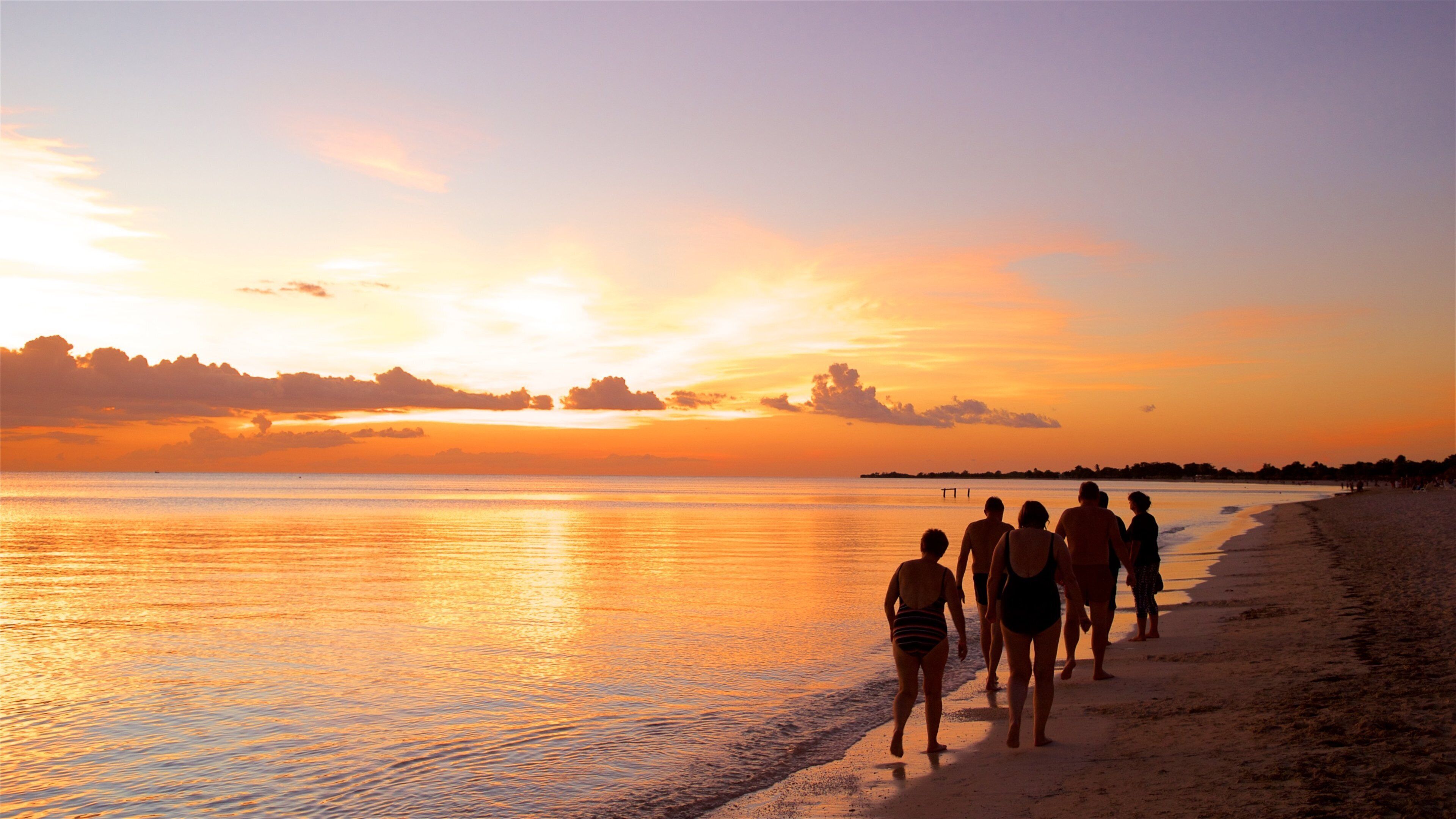 Un coucher de soleil sur une plage, avec des personnes se promenant le long du rivage.
