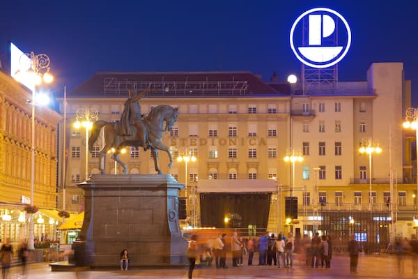 Estátua de um homem a cavalo numa praça, com um edifício identificado como 'STEDIONICA' ao fundo.