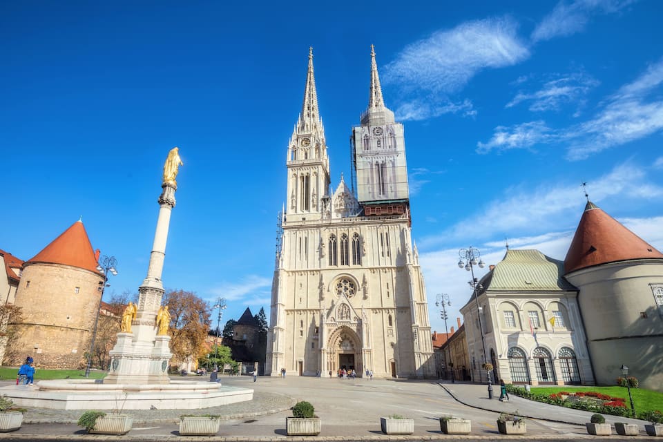 A cathedral with twin spires, a central tower, and a statue on a pedestal.