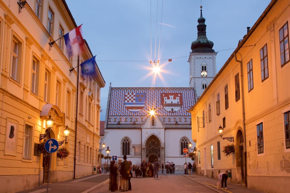 A historic street with buildings, a clock tower, and flags.