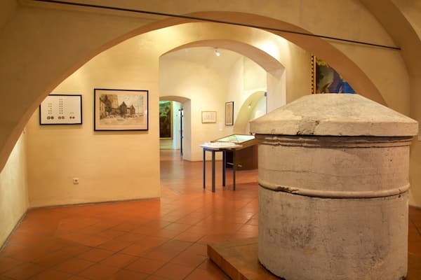 Um museu em ambiente interno com tetos em arco, pisos de azulejos e diversas obras de arte expostas nas paredes.