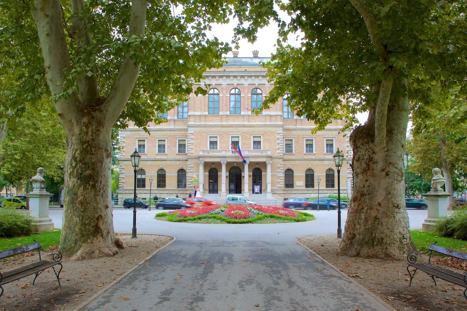 A building with a central entrance, flanked by trees and benches.