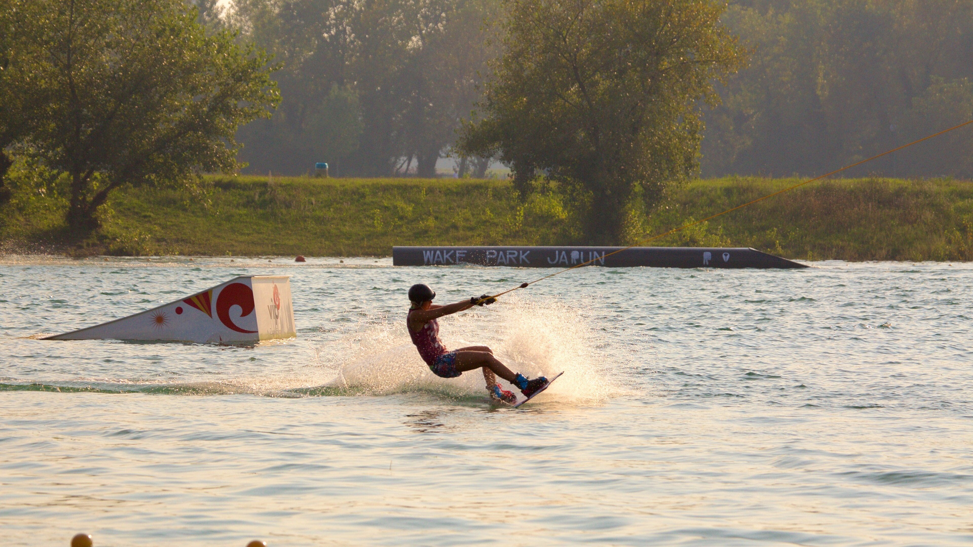 A wakeboarder performing a jump over a wakeboard ramp at Wake Park.