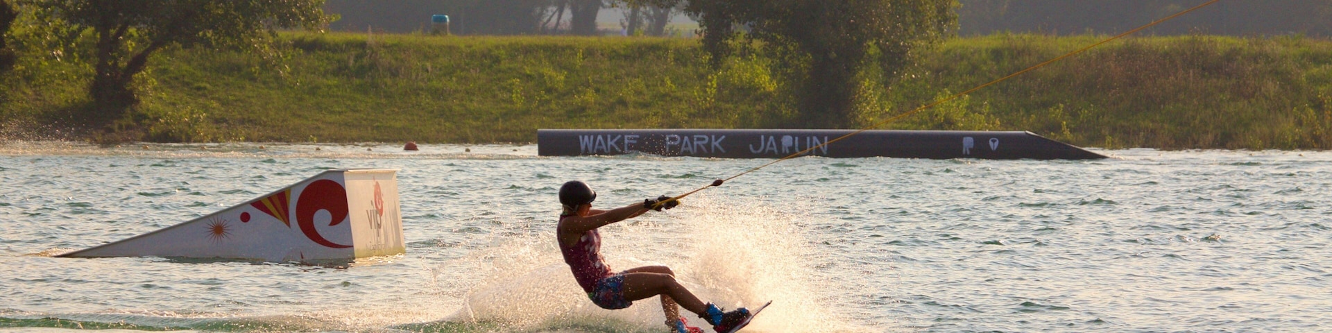 Practicante de wakeboard realizando un salto sobre una rampa en Wake Park.