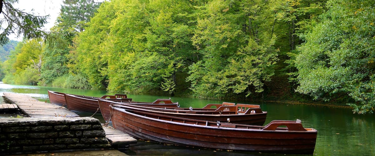 Wooden boats docked at a stone pier by a river surrounded by dense green foliage.