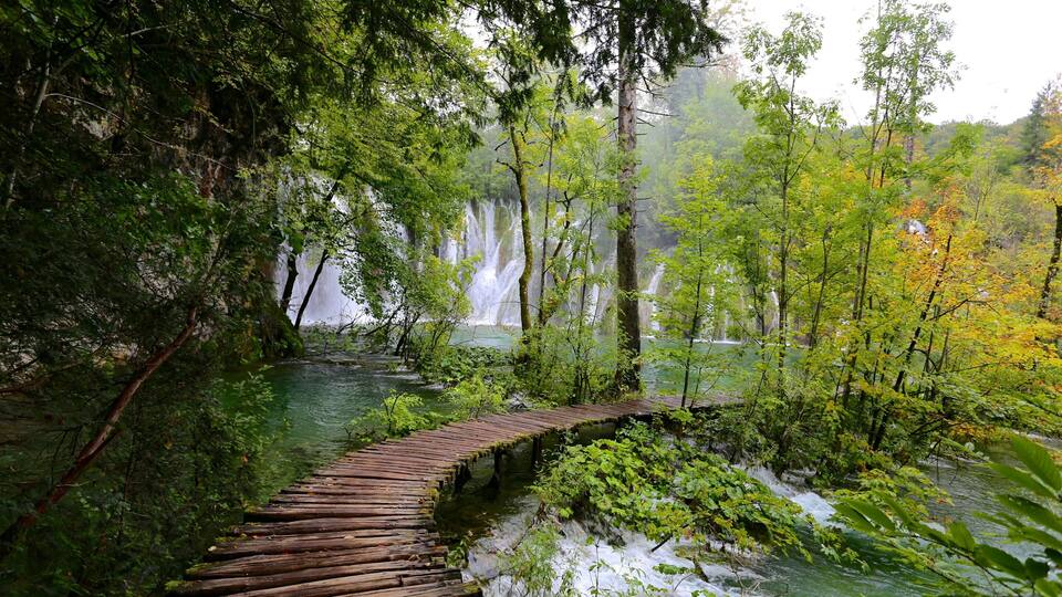 A wooden bridge over a river with waterfalls in the background.