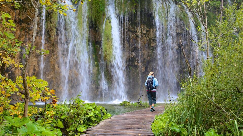 A hiker on a wooden boardwalk beside a waterfall.