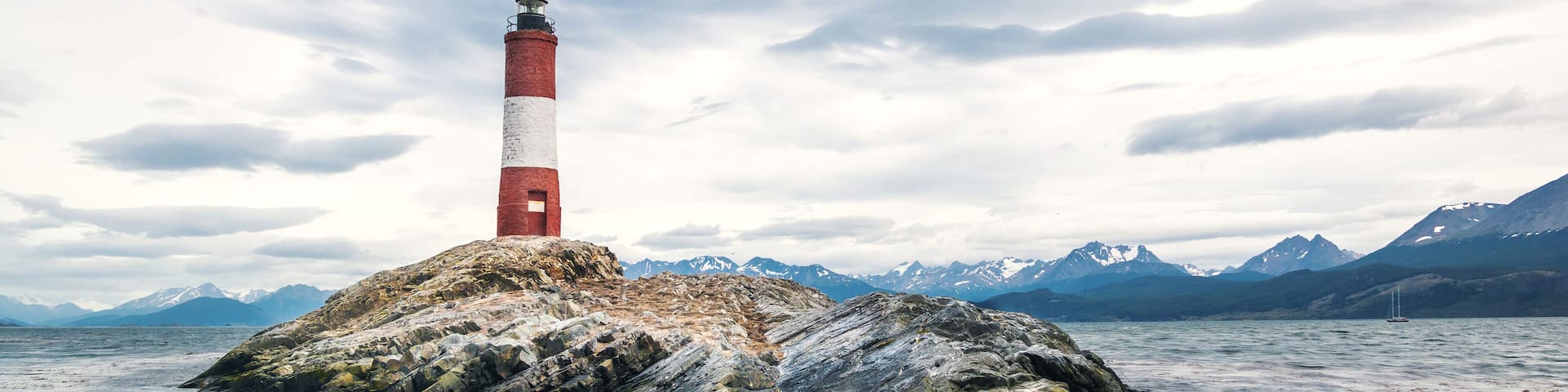 A lighthouse on a rocky island with mountains in the background.