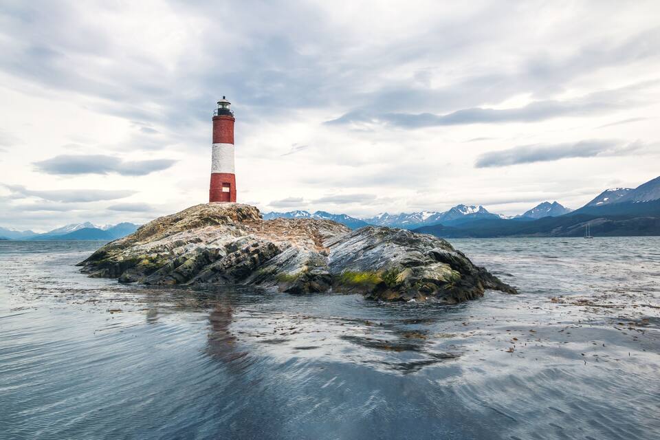 A lighthouse on a rocky island with mountains in the background.