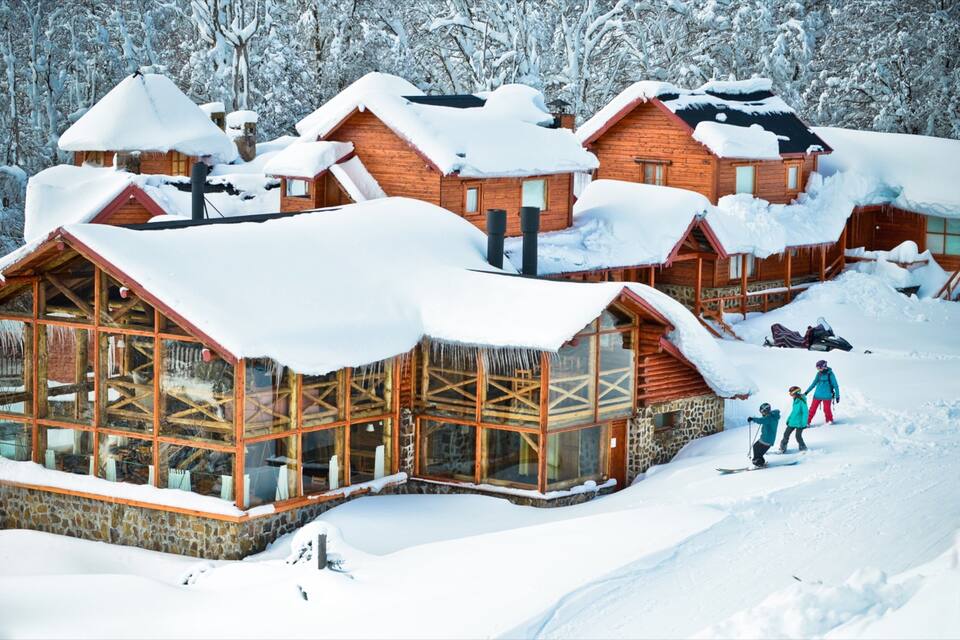 Una cabaña de madera con fachada de vidrio rodeada de árboles cubiertos de nieve.