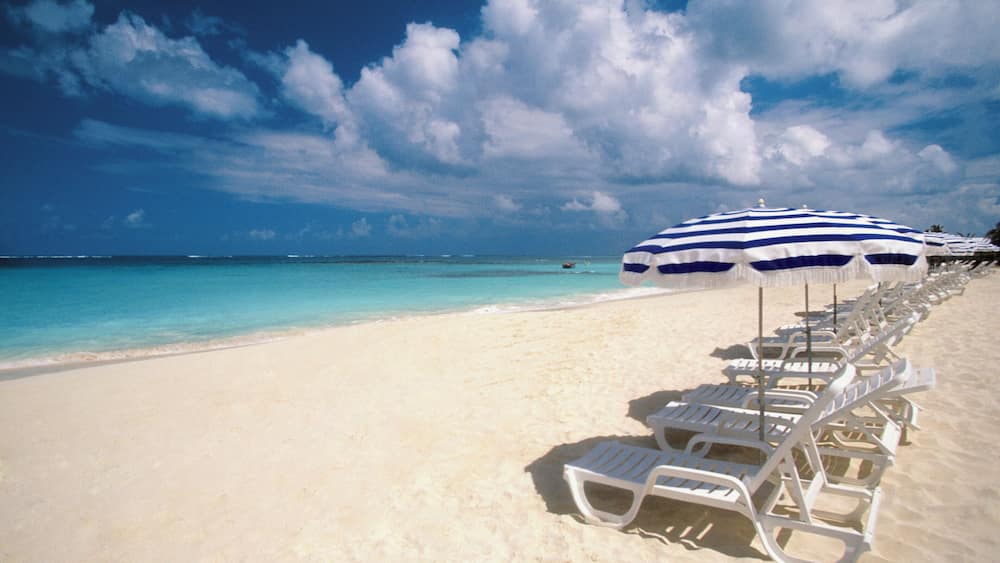 Many umbrellas and white lounge chairs in a line on Shoal Bay Beach on Anguilla, Caribbean