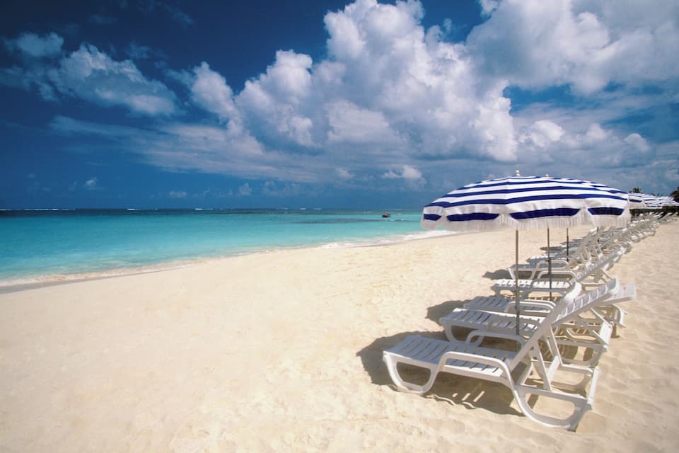 A beach with white lounge chairs and blue umbrellas, a clear sky, and turquoise water.