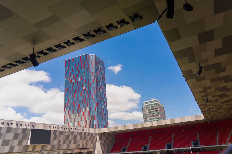 Un estadio con asientos rojos y un edificio moderno con fachada a cuadros.