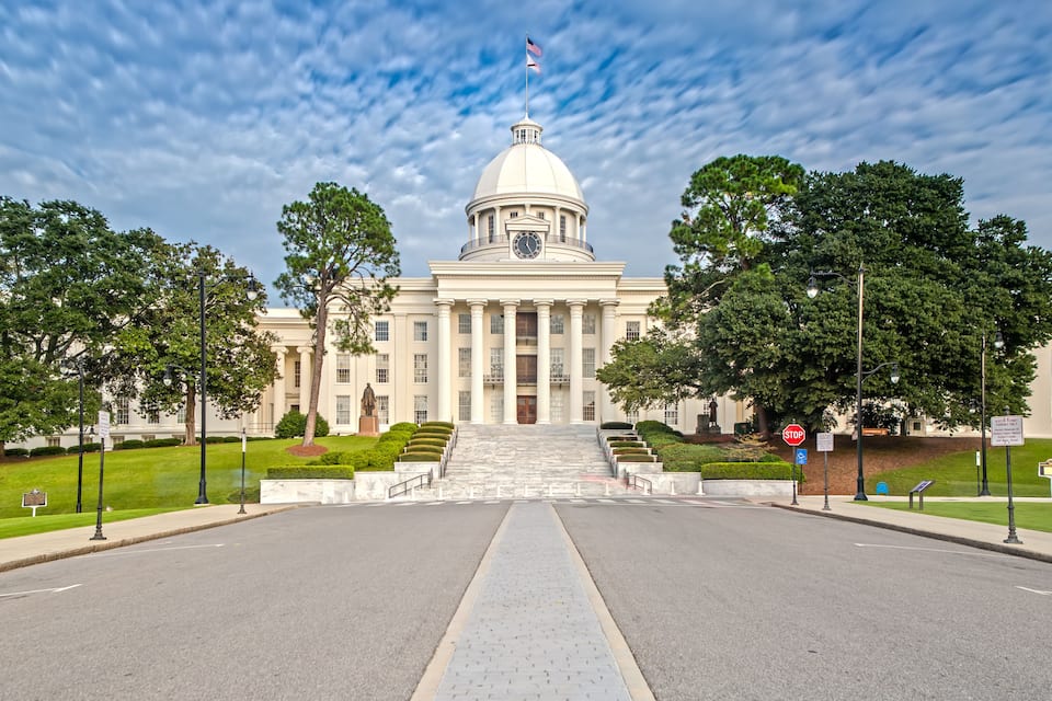 A large neoclassical building with a dome, a clock, and a flag on top.