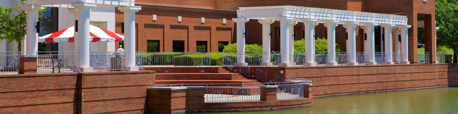 A brick building with white columns and a covered walkway by a body of water.
