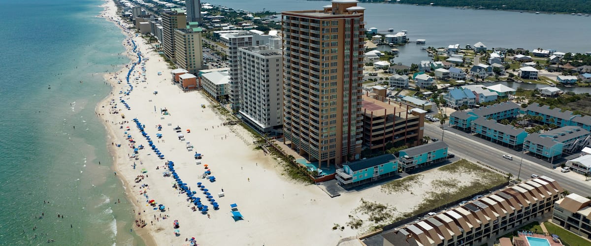 A coastal cityscape with a long sandy beach, high-rise buildings, and a marina.