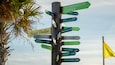 Un panneau indicateur directionnel comportant plusieurs panneaux pointant vers différentes destinations, comme le pavillon de la plage, Orange Beach, le pavillon de la forêt, et d’autres lieux.