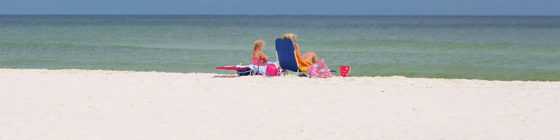 A beach with two people sitting on beach chairs, a clear sky, and calm ocean waters.