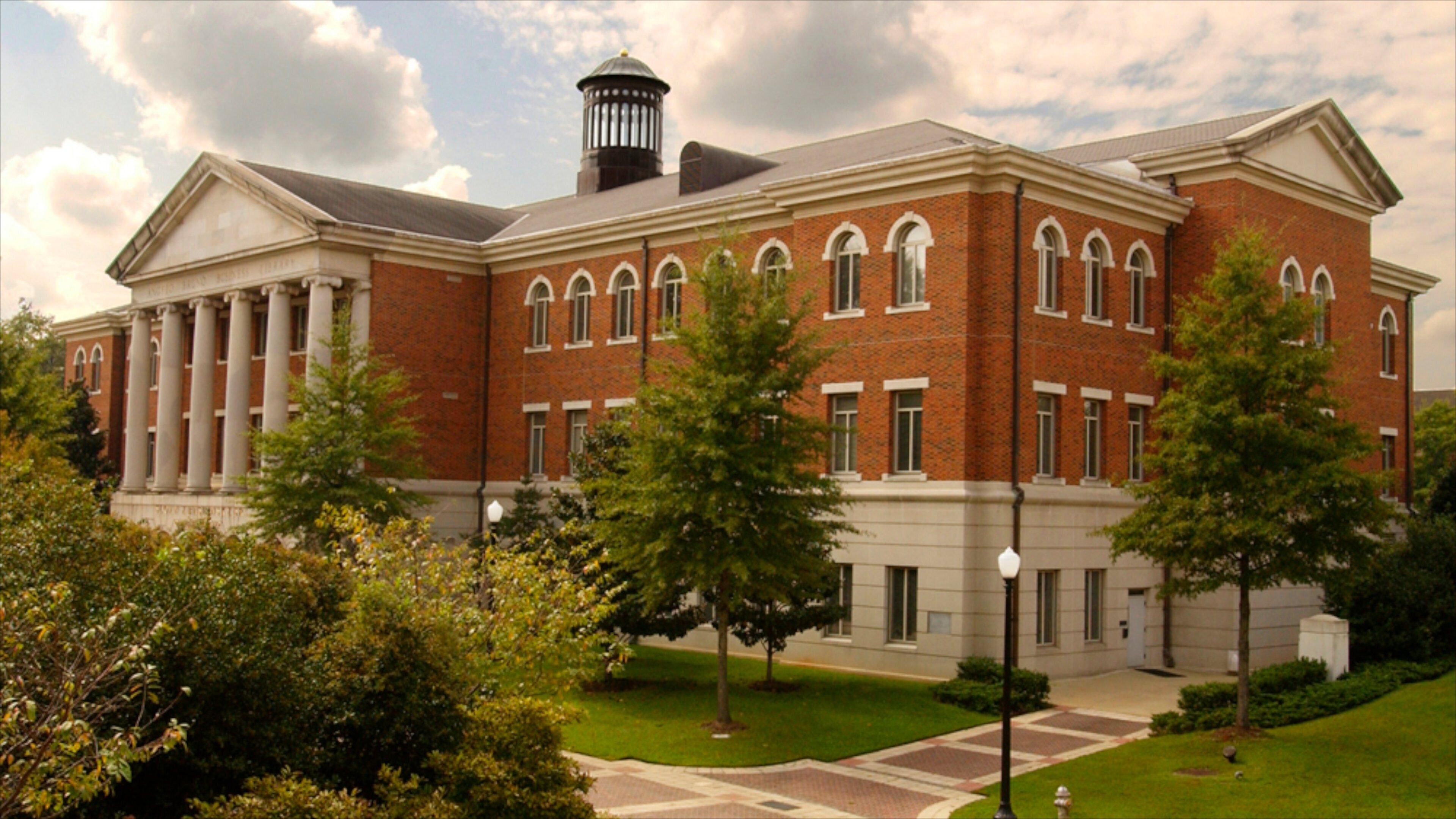 A large brick building with columns and arched windows, surrounded by trees and a well-maintained lawn.