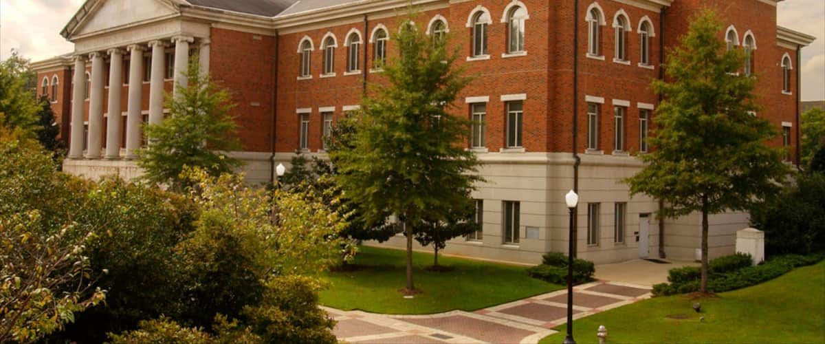 A large brick building with columns and arched windows, surrounded by trees and a well-maintained lawn.