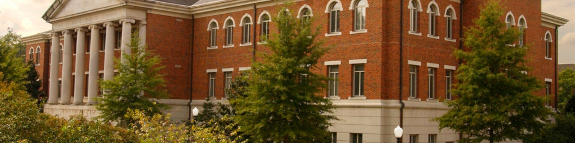 A large brick building with columns and arched windows, surrounded by trees and a well-maintained lawn.