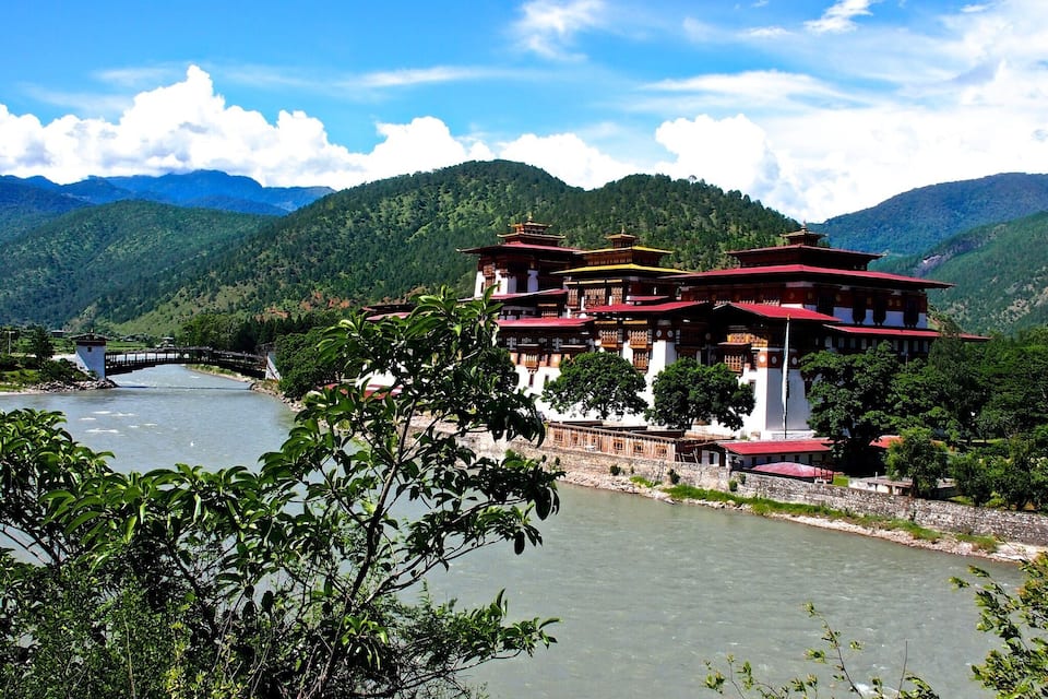 Un complexe de temples traditionnel à plusieurs niveaux, situé au bord d’une rivière et entouré de collines verdoyantes.